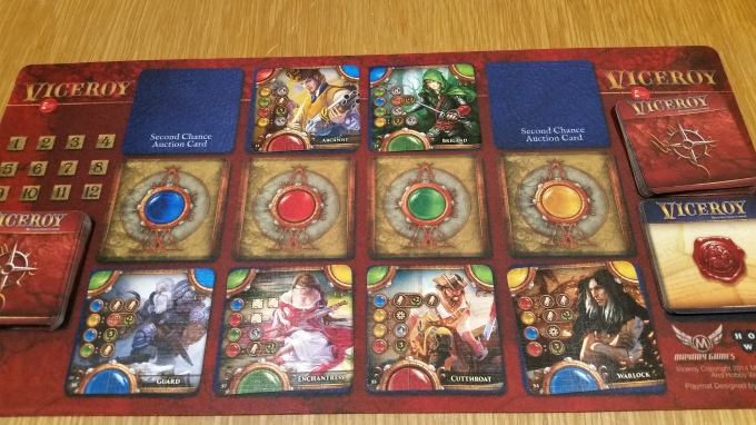 The setup for an auction. The characters above the red and green gems weren't grabbed last round, so they are in the second-chance slot. This shot features the optional, but awesome, playmat, not included in the base game.